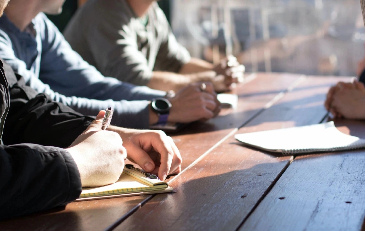 A group of people sitting at a table writing.