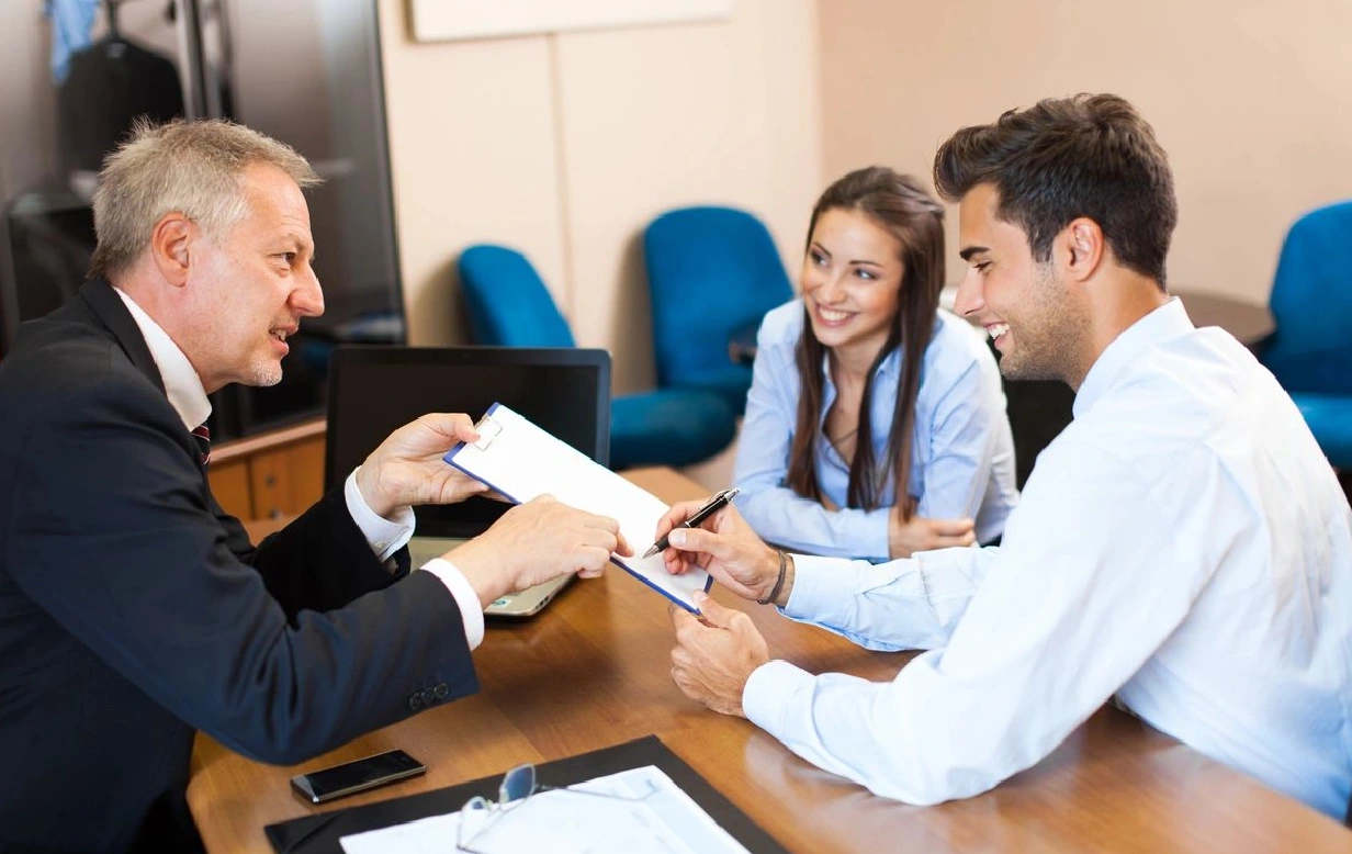 A man handing over papers to two people.