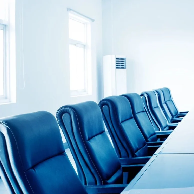 A row of blue chairs in front of a long table.