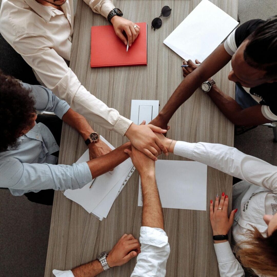 A group of people sitting at a table with their hands together.